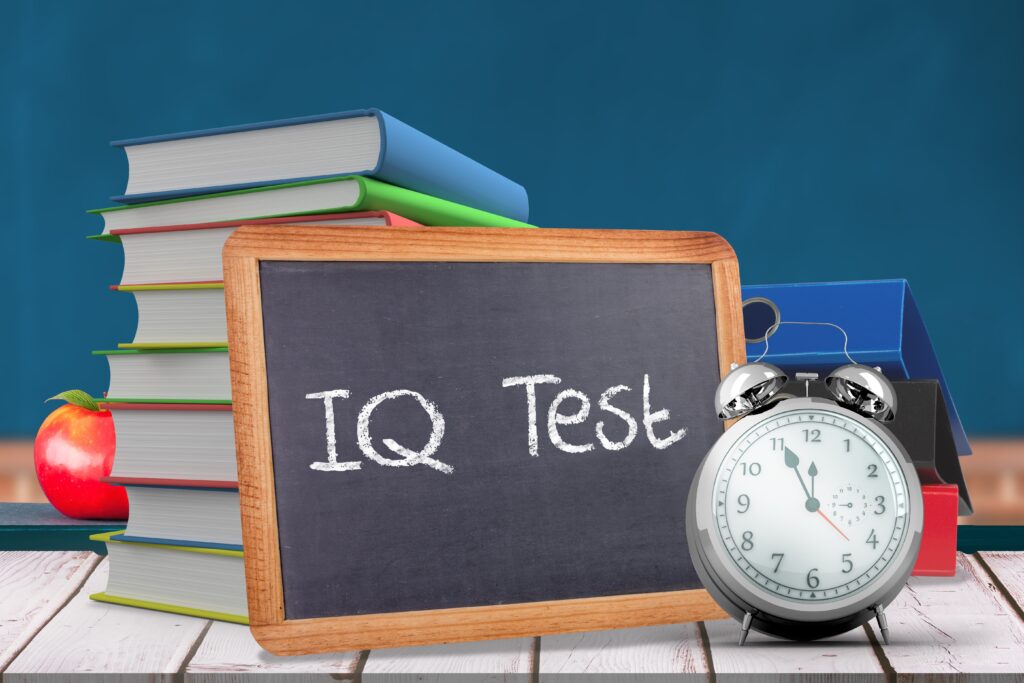 A photo of a stack of books with a chalk board leaning showing the words IQ Test